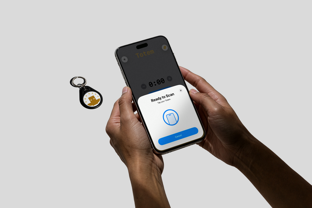 Someone holding a phone with Totem Focus app tapping our white keychain Totem with a yellow logo on a gray background. Used to aid focus for ADHD and students. Totem Focus.